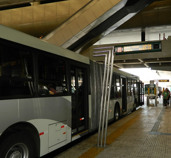 #pracegover lateral de ônibus articulado dentro de terminal perto de plataforma