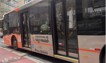 #pracegover ônibus da área oito ao lado de ciclovia com um prédio na frente
