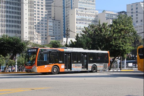 #pracegover lateral de ônibus laranja, da área oito, com prédios ao fundo