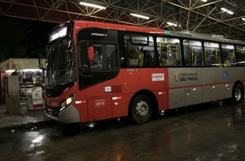 #pracegover ônibus vermelho dentro de terminal com a pista molhada