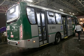 #pracegover lateral do ônibus da área cinco verde dentro do terminal com asfalto molhado porque da chuva