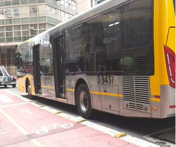 #PraCegoVer: Imagem diurna de um coletivo de cor amarela, em operação, no centro da cidade, ao lado de uma ciclovia
