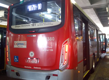 #PraCegoVer: Imagem da traseira de um ônibus estacionado em seu Terminal, com a porta dianteira aberta, aguardando o embarque dos passageiros.