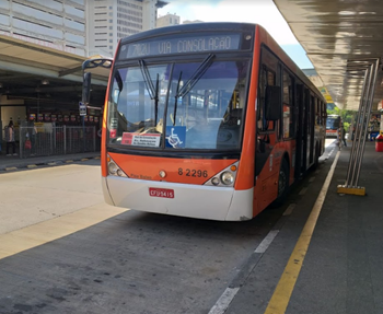 #PraCegoVer: Imagem diurna de um veículo de cor laranja, estacionado em seu terminal, com letreiro indicando a linha "702U-10 Cidade Universitária - Terminal Parque Dom Pedro"