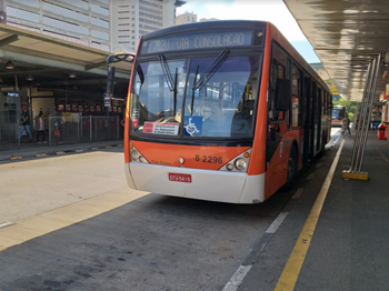 #PraCEgoVer: Imagem diurna de um veículo de cor laranja, que atende a Zona sudoeste, que opera a linha 702U, estacionado em seu Terminal.