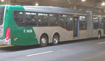#PraCegoVer: Imagem de um veículo de cor verde e cinza, estacionado em seu terminal, com usuários em seu interior.