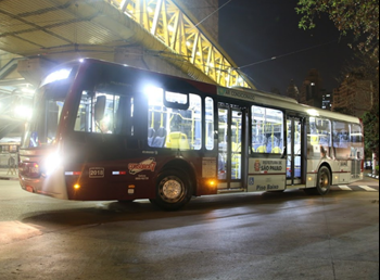 #pracegover a noite e ônibus da cor vermelha entrando em terminal
