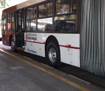 #PraCegoVer: Imagem de um ônibus de cor bordô, articulado, estacionado em seu Terminal, com portas dianteiras abertas, aguardando início de operação
