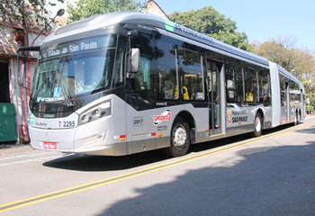 #PraCegoVer: Imagem de um ônibus de cor prateada, em operação de tarde pela cidade