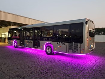 #PraCegoVer: Imagem de um ônibus cinza, em sua garagem com luzes de neon rosa na parte inferior do veículo