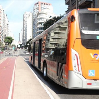 #pracegover parte da traseira do ônibus da gato preto ao lado uma ciclofaixa e logo a frente avenida com um carros
