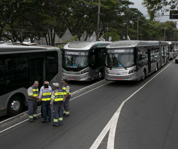#pracegover duas fileiras de ônibus prata letreiro expresso f1 com fiscais ao lado