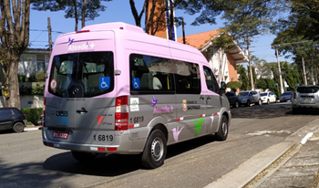 #pracegover van prata e rosa do atende+ em rua com carros estacionados casas e arvores