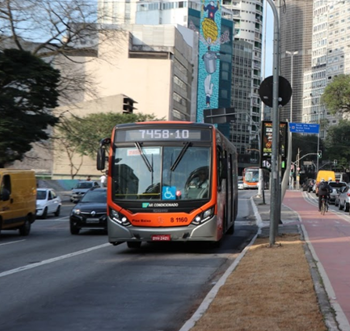 #PRACEGOVER ônibus da área oito cor laranja linha sete quatro cinco oito barra dez em avenida perto de carros e ciclofaixa com relógio digital